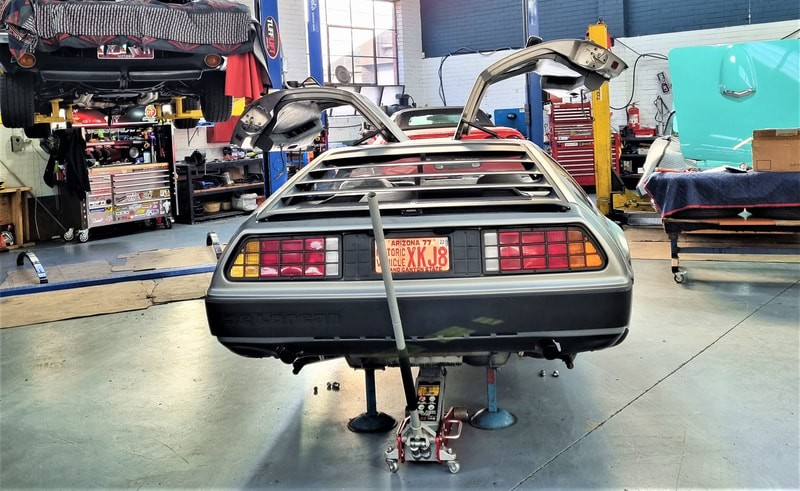 A Delorean car sits on a jack inside the TGS Muscle Cars workshop, where it is being modified and repaired.