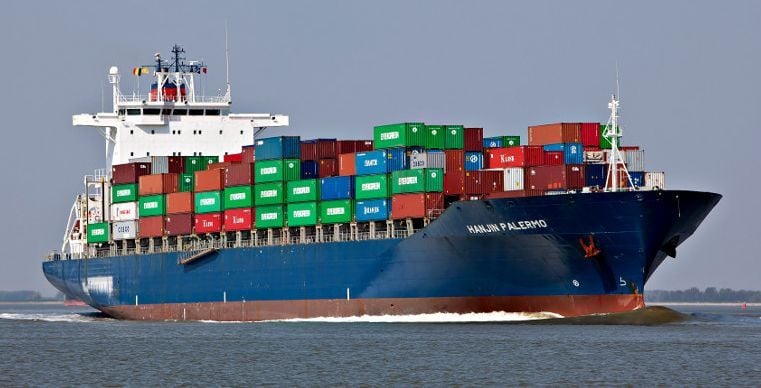 A large shipping freighter carries several shipping containers across the ocean.